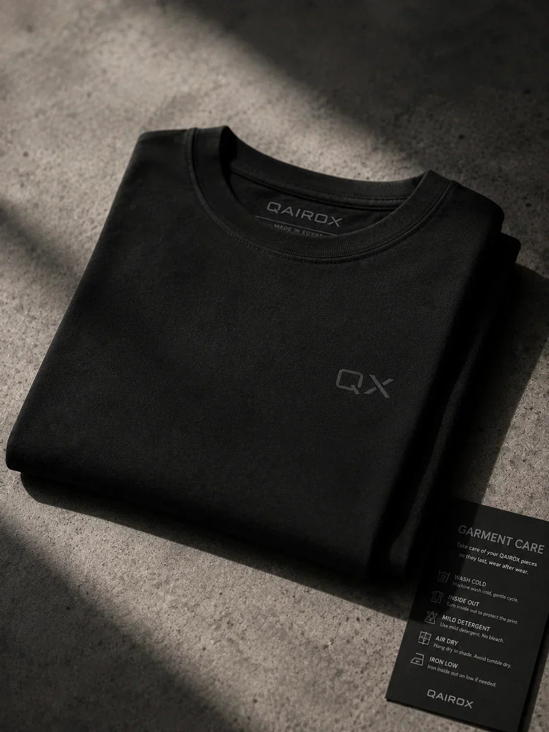 Neatly folded QAIROX premium cotton tee displayed on minimal dark surface