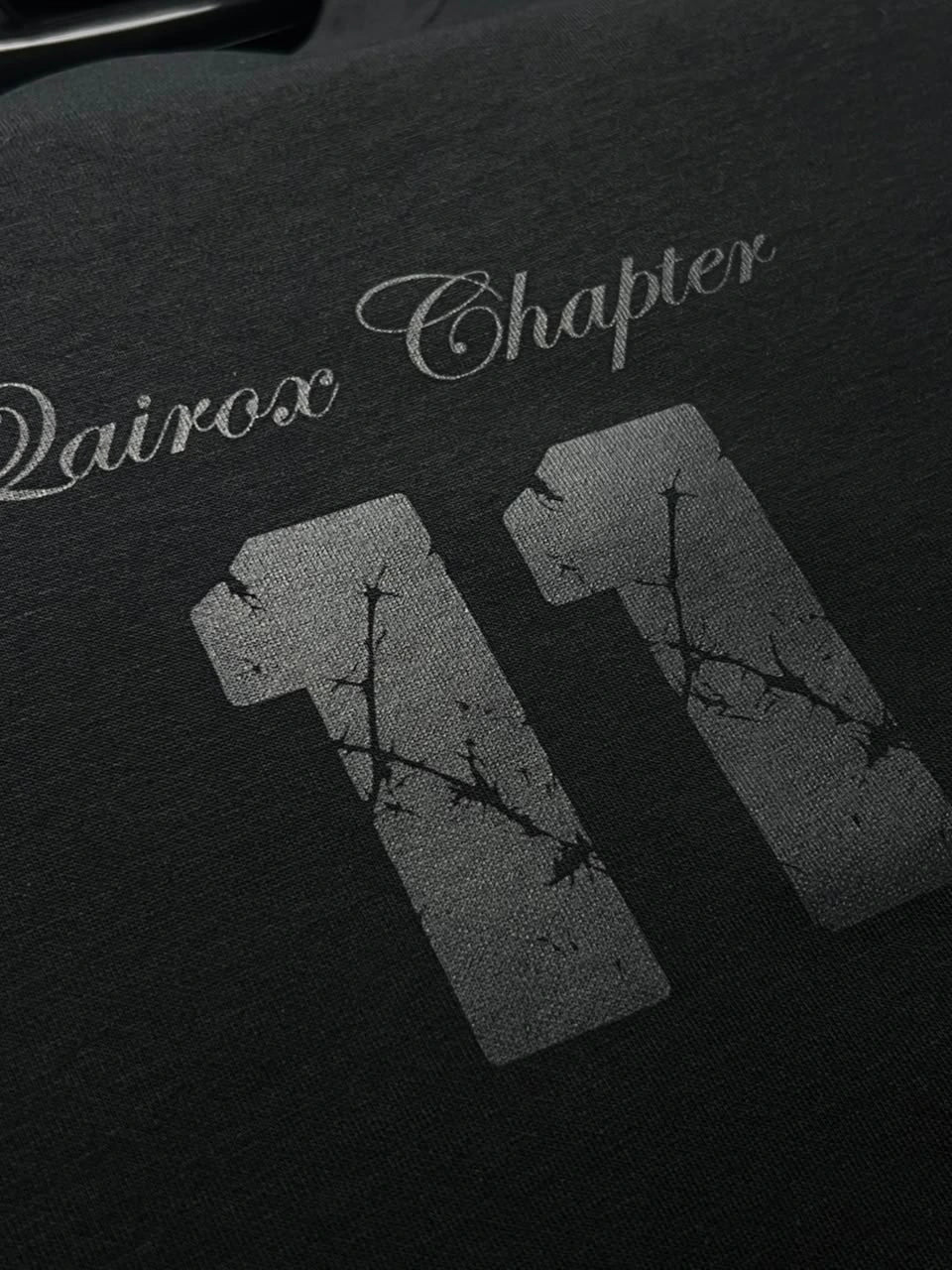 QAIROX Chapter Tee close-up — Qairox Chapter script with cracked texture 11 graphic, premium screen print detail on black cotton
