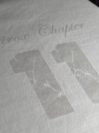 QAIROX Chapter Tee off-white close-up — subtle tone-on-tone Qairox Chapter 11 graphic detail, premium screen print on cotton interlock