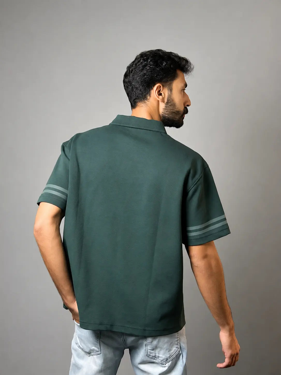 A man wearing a dark green short-sleeve polo shirt with light gray sleeve stripes, shown from the back against a solid gray background.