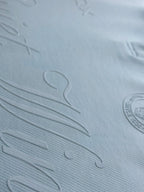 Close-up of a light blue textured fabric with embossed script lettering and a circular logo on the right side.